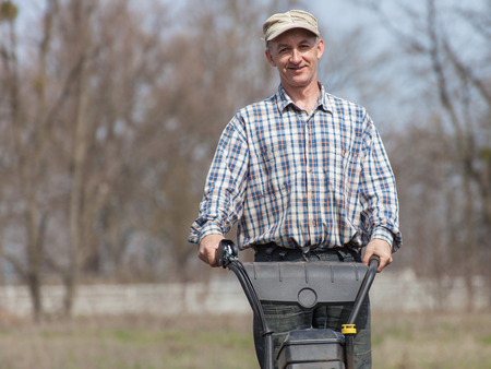 Portrait of smiling farmer. Man working in the garden with garden tiller. Man with tractor cultivating field at spring. Farmer loosens soil by petrol cultivatorの写真素材