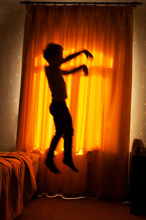 Sleepwalker boy jumps from bed in the moonlit window background, blurred motionの写真素材