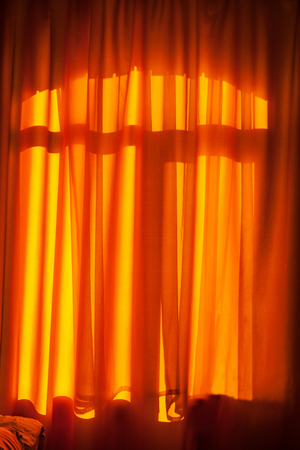 Orange curtain closes the window illuminated by sunlightの写真素材