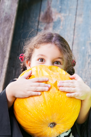 Halloween and celebration concept. Beautiful child girl in witch costume holds Halloween pumpkin outdoorsの写真素材