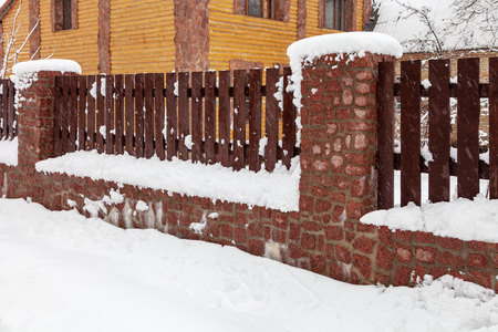 Wooden fence with a stone foundation covered with snow after a heavy snowfall in winterの写真素材