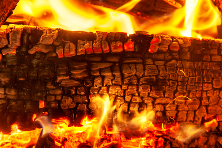 Burning log of wood close-up as abstract background. The hot embers of burning wood log fire. Firewood burning on grill. Texture fire bonfire embers. Smoldering fireの写真素材