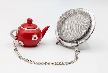 Tea strainer on white background and miniature teapot decoration on a chainの写真素材