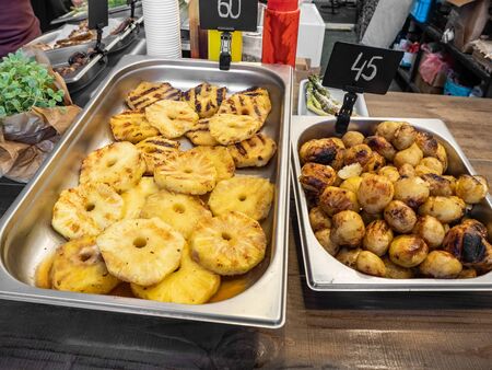 Grilled pineapple and potatoes in a stainless steel tray on the street food festival, close-up top viewの写真素材