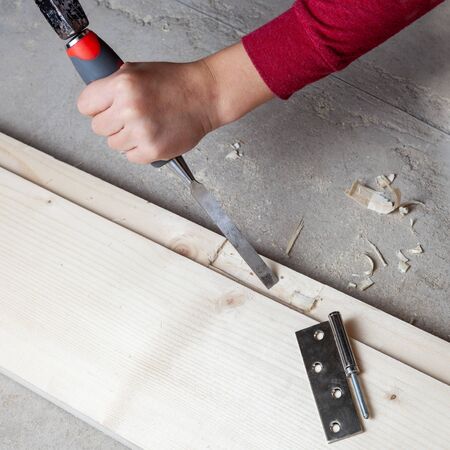 Chisel and hammer in the hands of a boy, install door hinges on a wooden door