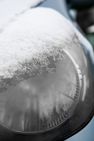 Car headlight covered with snow and ice, close-up. Automobile in winter day, snowstorm outdoorsの写真素材