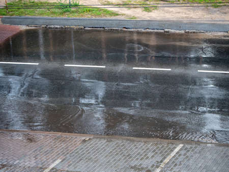 Heavy rain drops falling on city street during downpour, empty parking and the road with puddlesの写真素材