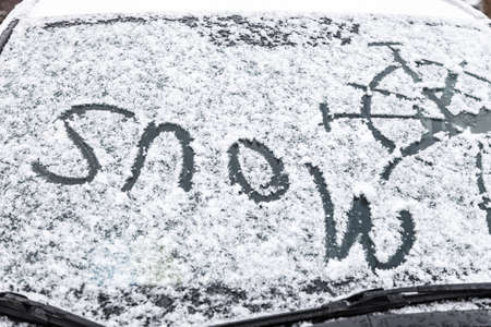 The inscription snow, on the surface of the car front windshield, covered with snowの写真素材