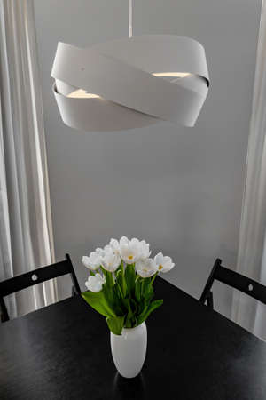 Bouquet of white tulips in a vase on a black table, a designer lamp above