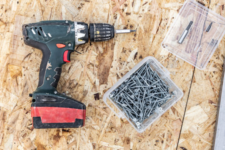 An electric screwdriver, a box of screws and bits are lying on the surface of the OSB plate
