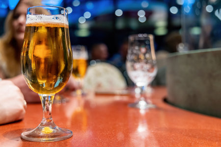 A glass of light beer in a dark pub stands on the rackの写真素材