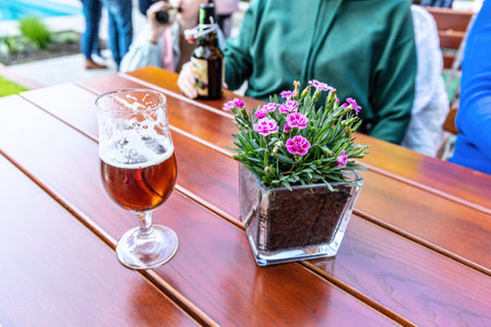 A glass of beer and a vase of flowers are standing on the tableの写真素材