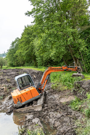 An excavator clears a silted lake, which is overgrown with reedsの写真素材