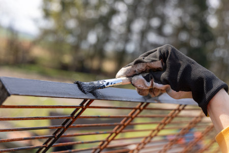 A woman is painting a metal grid with black paint outdoorsの写真素材