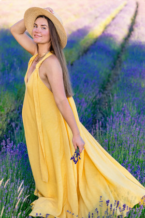 A pregnant woman in a yellow dress is standing on a blooming lavender fieldの写真素材