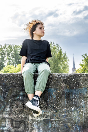 The girl is sitting on a concrete wall, behind her is a blue skyの写真素材
