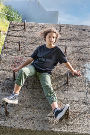 The girl is sitting on a concrete wall, behind her is a blue skyの写真素材