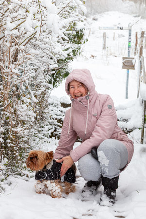 A woman holds a Yorkie dog during a walk in winterの写真素材