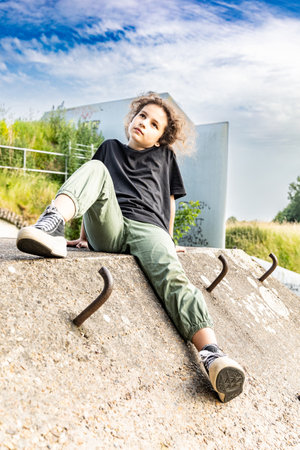 The girl is sitting on a concrete wall, behind her is a blue skyの写真素材