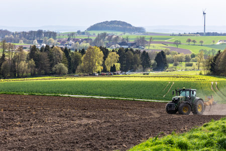 Tractor cultivates plowed field in spring, agricultural landscape