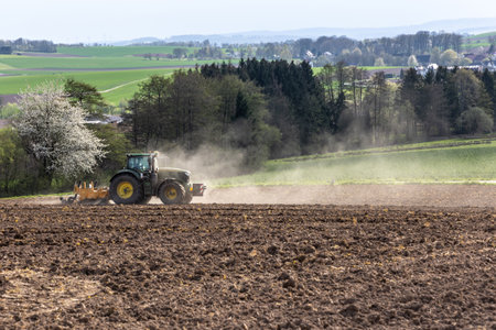 Tractor cultivates plowed field in spring, agricultural landscape