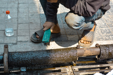 Worker washes a metal pipe with a brush in the street.