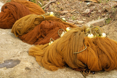 Brown fishing nets with floats, placed neatly on gravel dirt ground used by fishermen.
