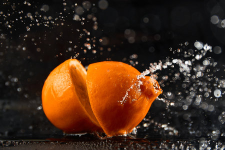Falling orange halves with splashing water on blackの写真素材