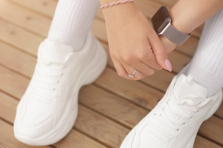 An athletic girl in white leggings and white sneakers is resting after jogging in a city park. Black watch with a silver strap on the armの写真素材