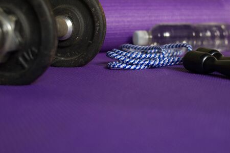 dumbbell, jump rope and bottle of water on violet matの写真素材