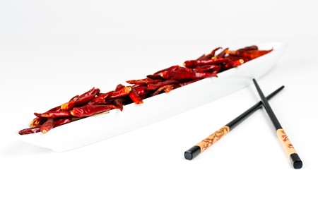 Two chopsticks next to a bowl of dried chili fruitsの写真素材