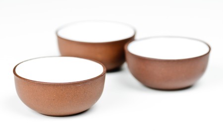 Brown clay tea cups on a white background. Focus on the one closest to camera.の写真素材