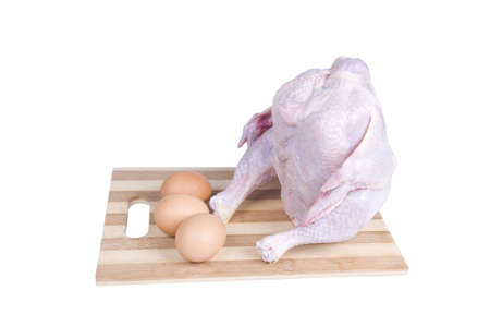 Raw chicken sitting on a board with eggs isolated over whiteの写真素材