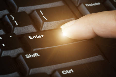 Closeup view of  finger press the enter key button on black computer keyboard with light flareの写真素材