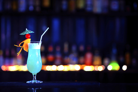 A glass of alcoholic cocktail on a bar counter with colorful bokeh background with copy spaceの写真素材
