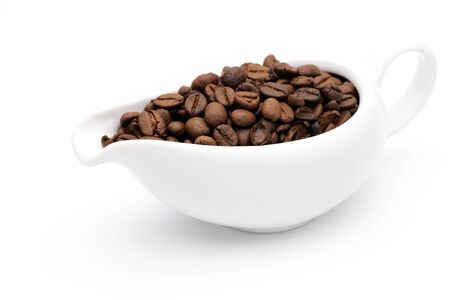 Coffee beans in a ceramic milk jug on white backgroundの写真素材