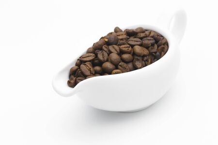 Coffee beans in a ceramic milk jug on white backgroundの写真素材