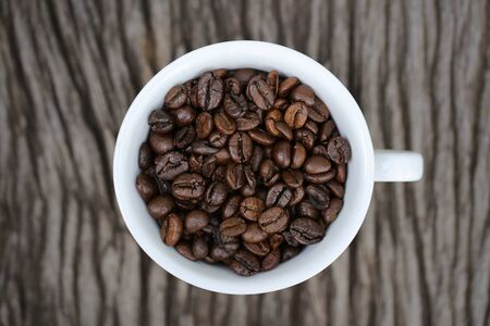 Coffee beans in a white coffee cup on wooden backgroundの写真素材