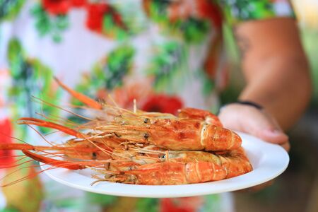 Man's hand holding the grilled shrimp on the white plate selective focusの写真素材
