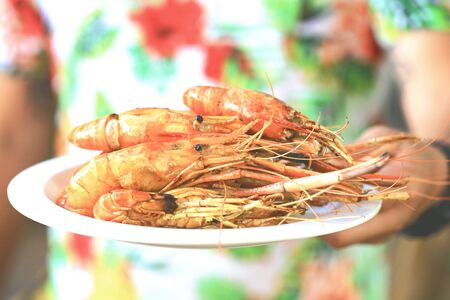 Man's hand holding the grilled shrimp on the white plate selective focusの写真素材