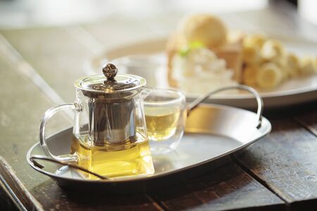 Transparent glass teapot and cup of tea on the stainless steel tray placed on the wooden tableの写真素材
