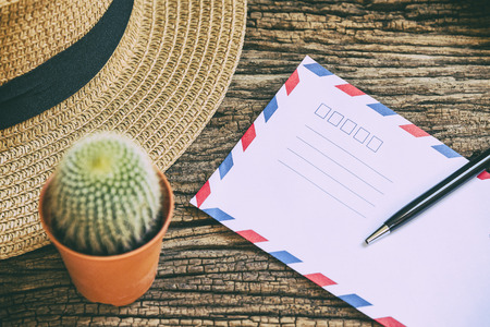 the envelop and the pen on the wooden background table with the hat and cactusの写真素材