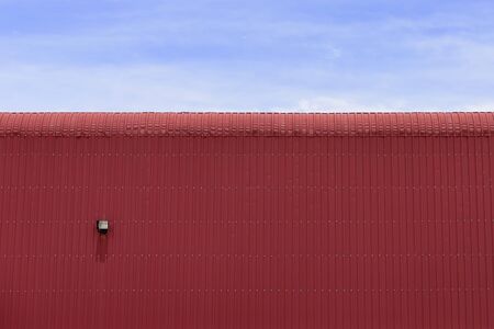 the factory building,the factory building made by sheet metal with the blue sky.The sheet metal roof of factory building with the sky.Close-up of the red factory building which made from sheet metal.の写真素材