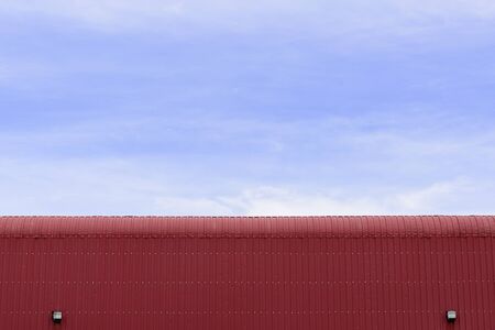 the factory building,the factory building made by sheet metal with the blue sky.The sheet metal roof of factory building with the sky.Close-up of the red factory building which made from sheet metal.の写真素材