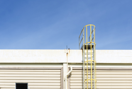 The yellow fire escape stair attach at the factory building with the blue skyの写真素材