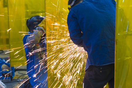 The welding craftsman grinding the steel tube and ware the safety mask.Heavy construction concept