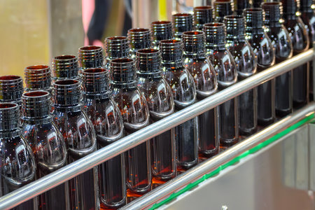 The dark brown bottles on the conveyor belt between filling process.  The pharmaceutical...