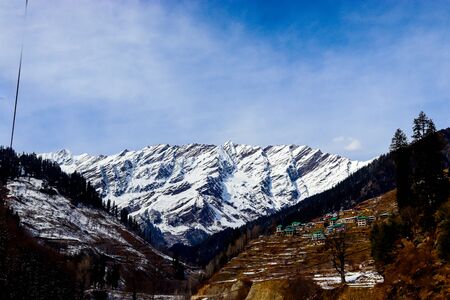 snow-covered mountain in the background with mountain covered with pine trees in the front.の写真素材