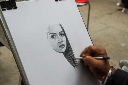 01 Janurary â2019, Rock Garden, Chandigarh, Punjab. A person drawing a sketch of girl on white paper with a pencil on white paper at Rock Garden, Chandigarh, Punjab, Indiaのeditorial素材