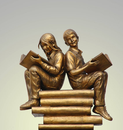 Brass statues of children reading a book sitting on a stack of books の写真素材